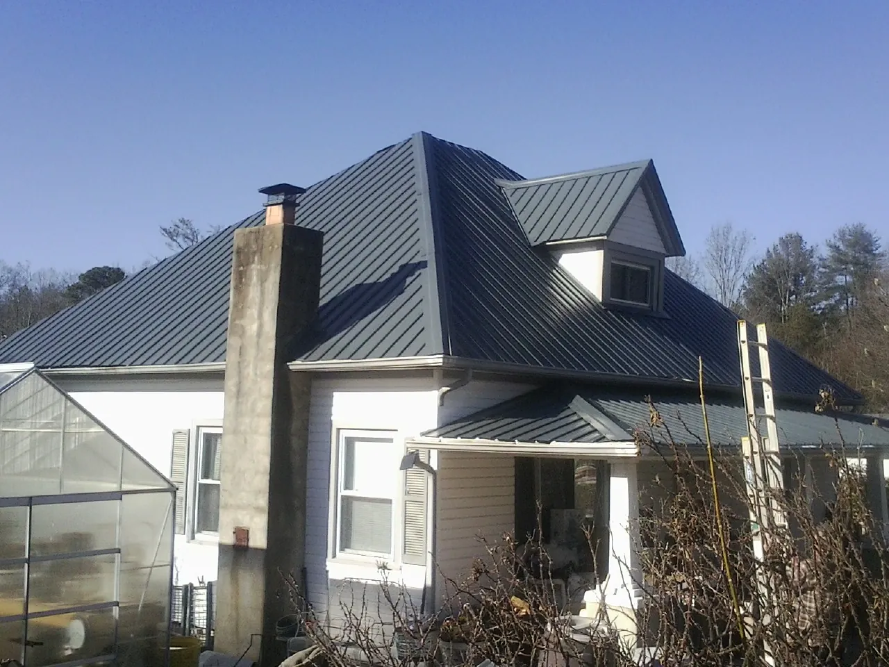 Dark blue standing seam metal roof on a white farmhouse with dormer — Slate & Tile Roof Repair by Roofing Brothers in Lidgerwood