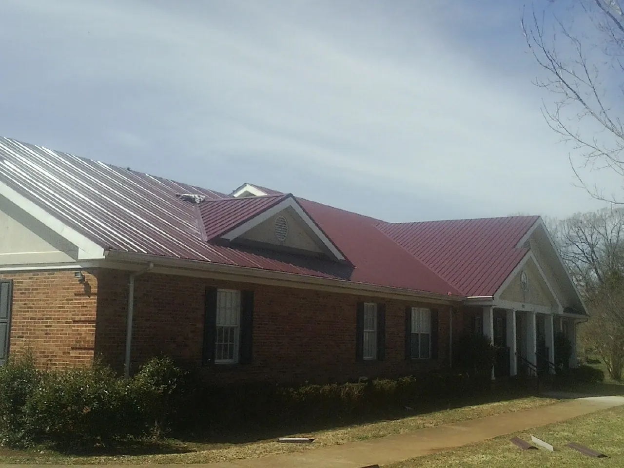 Red metal roof with gabled entries on a long brick building, from a Hail Damage Roof Repair job in Lidgerwood