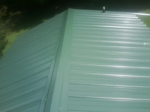 New green metal panels meeting at the ridge of a roof — Flat Roof Repair work by our crew in Lidgerwood