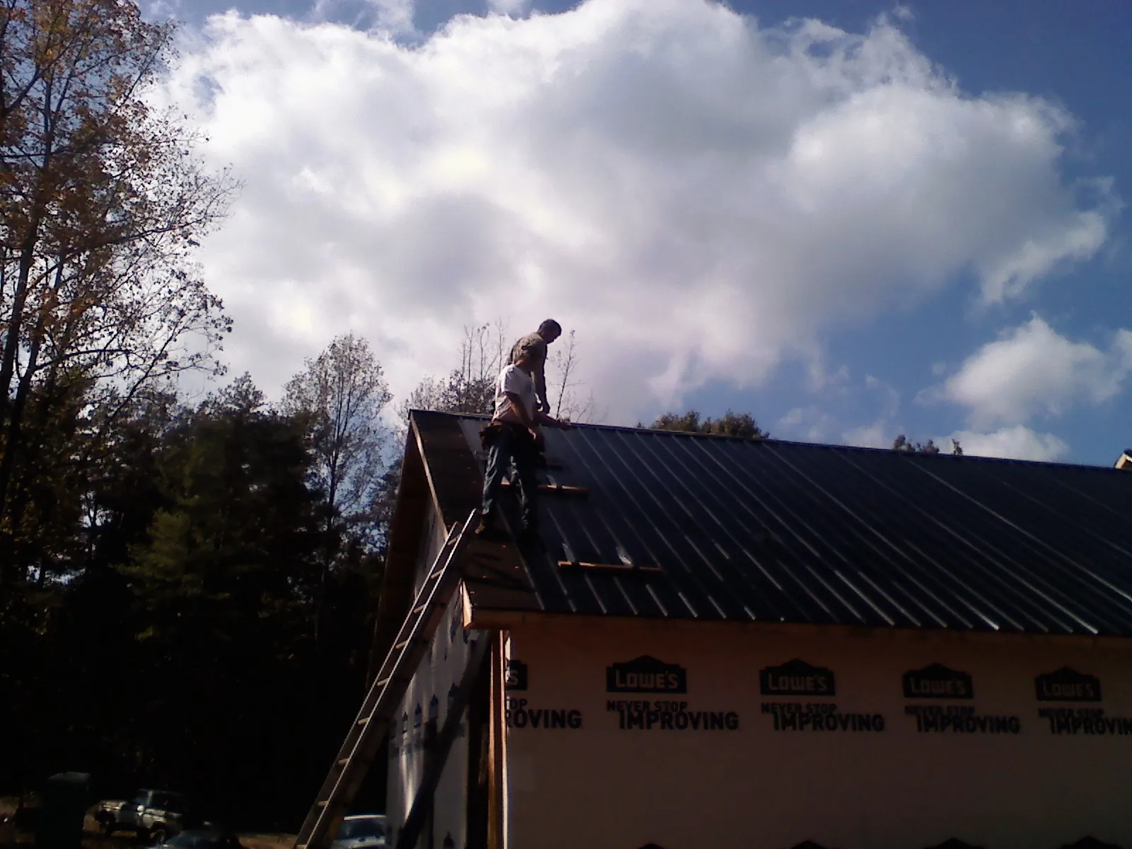 Roofer fastening dark metal panels high against a cloudy sky, from a Roof Inspection job in Lidgerwood