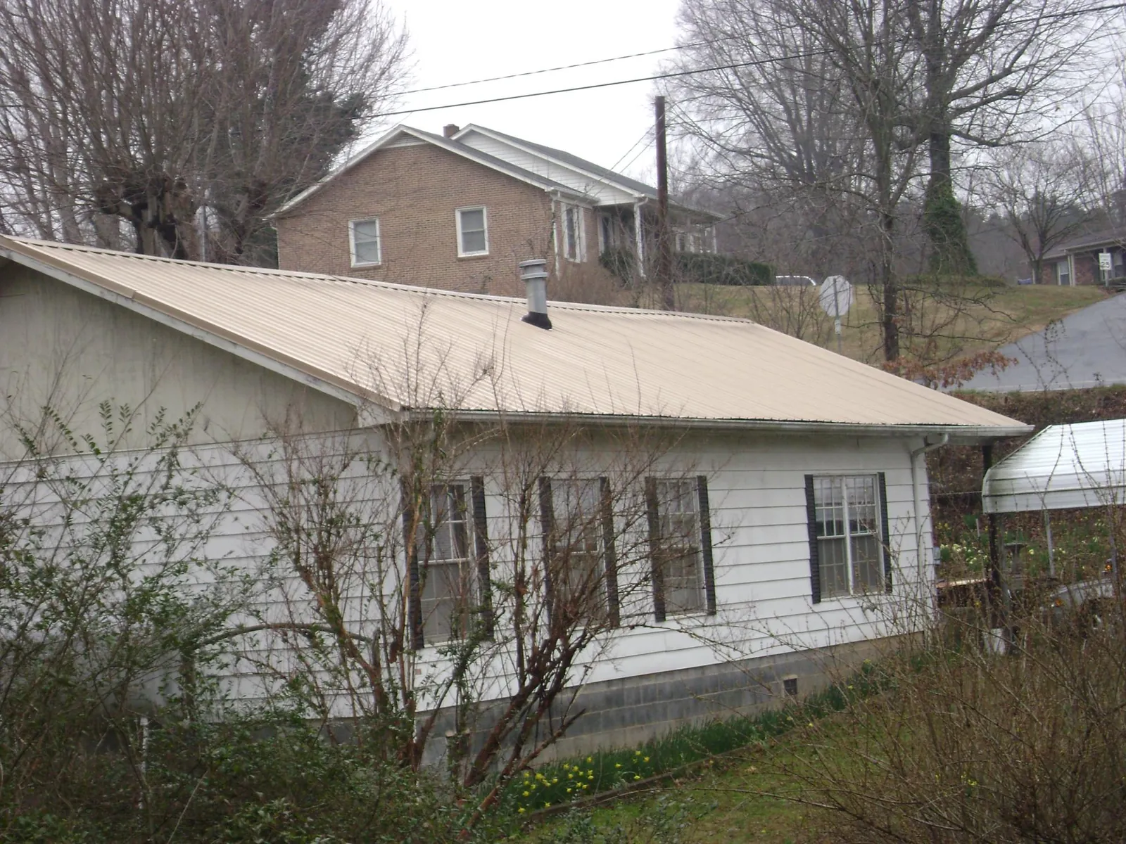 Tan metal roof on a white sided house set into a hillside — Commercial Roofing by Roofing Brothers in Lidgerwood
